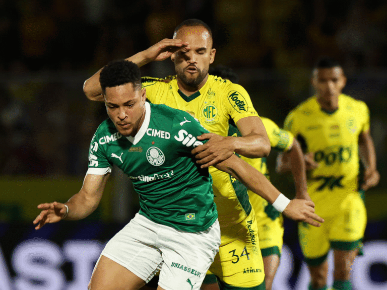 Jogador de futebol disputando lance forte em campo.