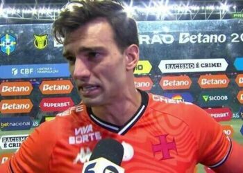 Jogador de futebol falando em entrevista, estádio ao fundo.