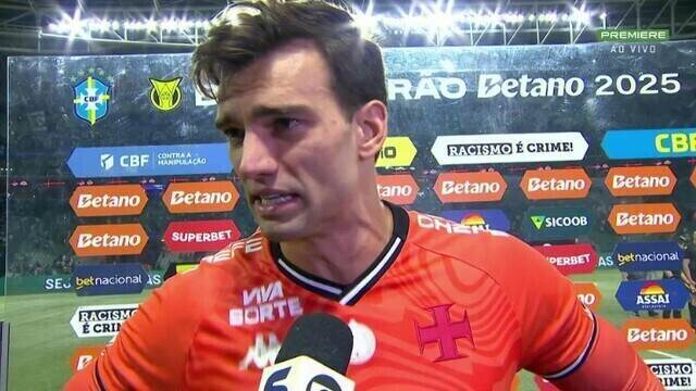Jogador de futebol falando em entrevista, estádio ao fundo.