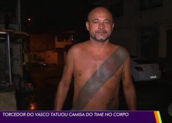Homem com tatuagem no corpo, sem camisa, na rua à noite.