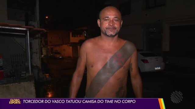 Homem com tatuagem no corpo, sem camisa, na rua à noite.