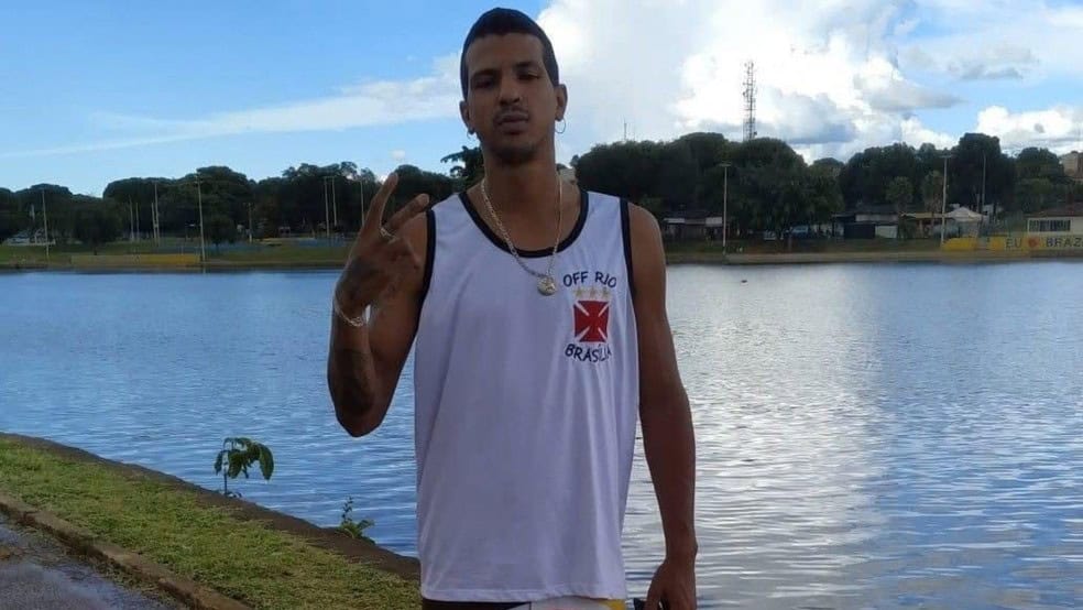 Vascaíno fazendo sinal de paz com lago ao fundo.