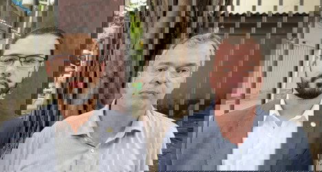 Homens em frente a barreiras de ferro e árvores.