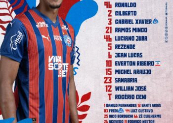 Vasco jogador com uniforme azul e vermelho, sorrindo.