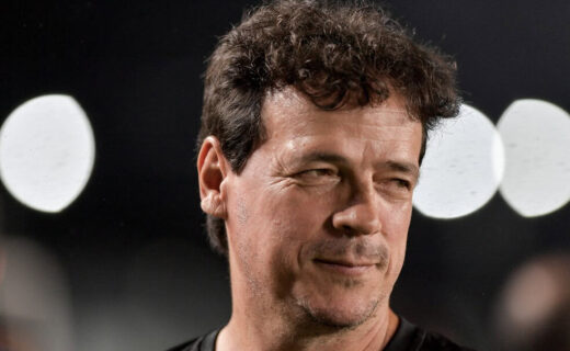 Homem sorrindo com cabelo castanho escuro e fundo de luzes brancas.