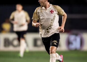 Jogador de futebol correndo com a bola em campo.