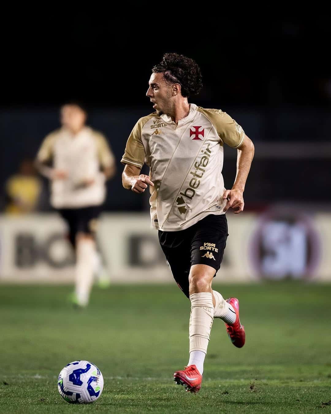 Jogador de futebol correndo com a bola em campo.