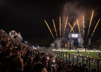 Festa no estádio com fogos de artifício e torcedores vibrando.