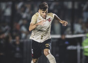 Jogador de futebol com uniforme do Vasco, controlando a bola em campo.