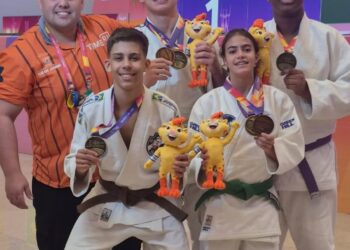 Medalhistas de judo com mascotes e treinador em cerimônia.