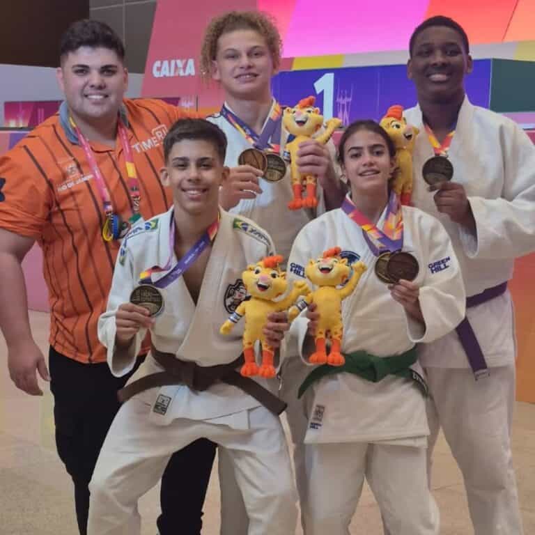 Medalhistas de judo com mascotes e treinador em cerimônia.