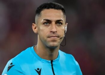 Jogador de futebol em uniforme azul com microfone na orelha.