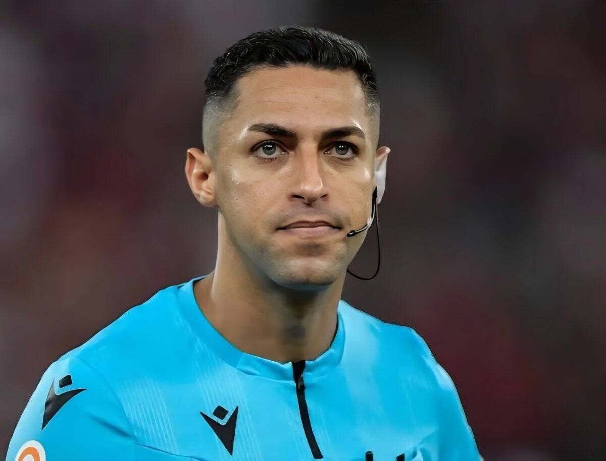 Jogador de futebol em uniforme azul com microfone na orelha.