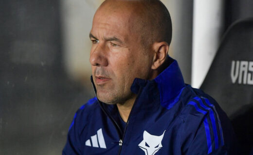 Homem com cabelo raspado e blusa azul com detalhes pretos.