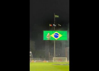 Bandeira do Brasil e estádio de futebol em noite chuvosa.