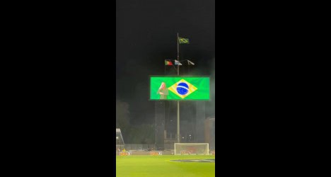 Bandeira do Brasil e estádio de futebol em noite chuvosa.
