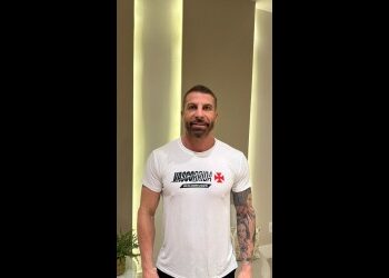 Homem com camisa branca e tatuagem visível.