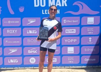 Corredora segurando troféu na praia, após corrida de revezamento.