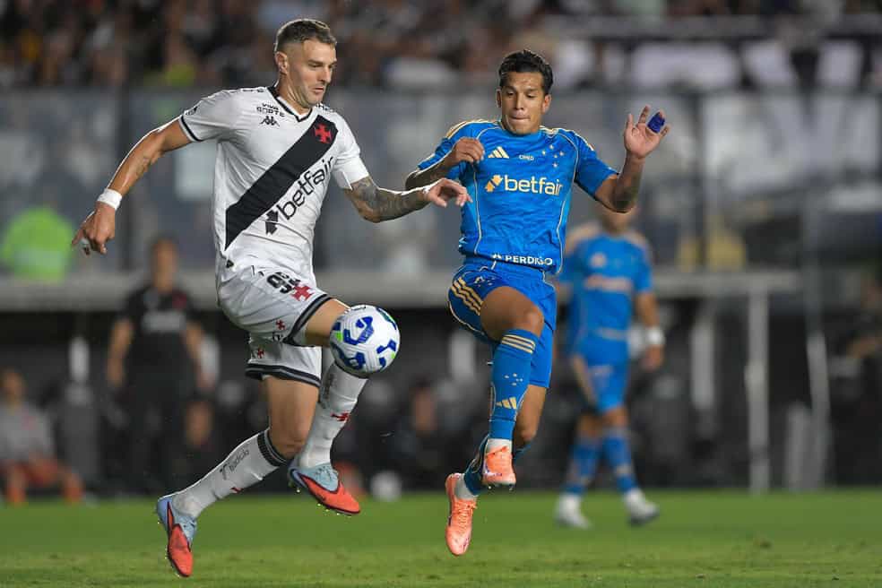 Jogadores do Vasco e adversário disputando a bola no campo.