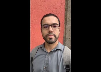 Homem com óculos e mochila against parede coral.