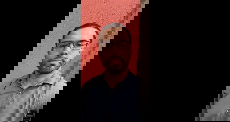 Homem com óculos e mochila against parede coral.