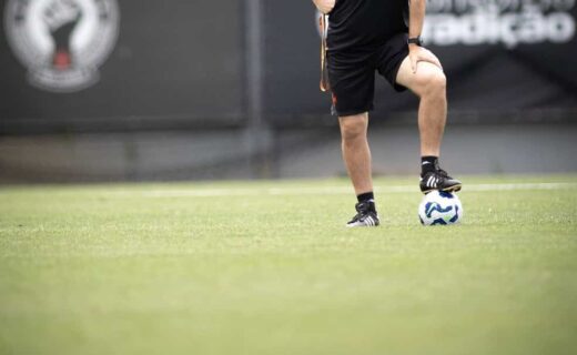 Futebolista treinando no campo com bola nos pés.