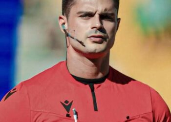 Árbitro de futebol com uniforme vermelho e microfone.