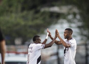 Jogadores comemorando gol, trocando high five em campo de futebol.