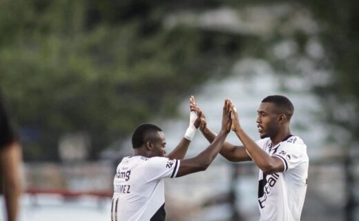 Jogadores comemorando gol, trocando high five em campo de futebol.