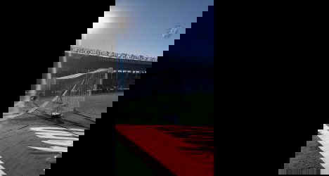 Futebol em campo com arquibancada ao fundo.