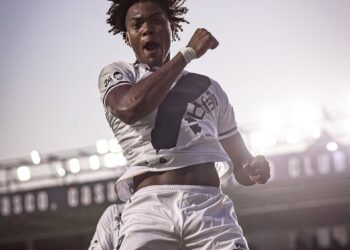 Jogador de futebol comemorando gol com expressão de vitória.