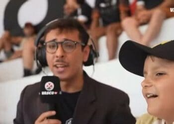 Locutor com microfone e menino sorridente em estádio.