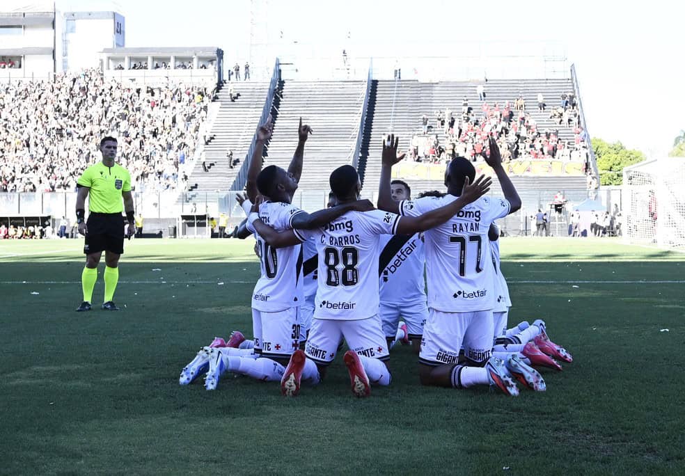 Narrador, jogadores do vasco comemorando gol em campo ao lado de torcida.