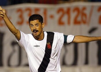 Jogador comemorando gol com braços abertos e expressão emocionante.