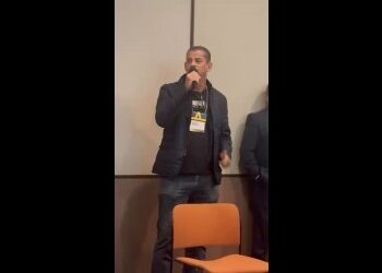 Homem falando ao microfone em evento.