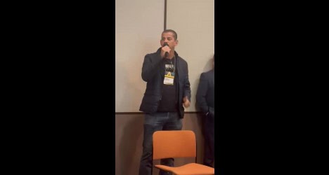 Homem falando ao microfone em evento.