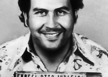 Homem sorridente segurando placa de prisão antiga.