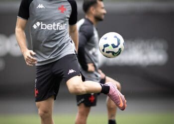 Jogador treinando com chuteira rosa, interceptando bola branca com detalhes azuis durante treino.