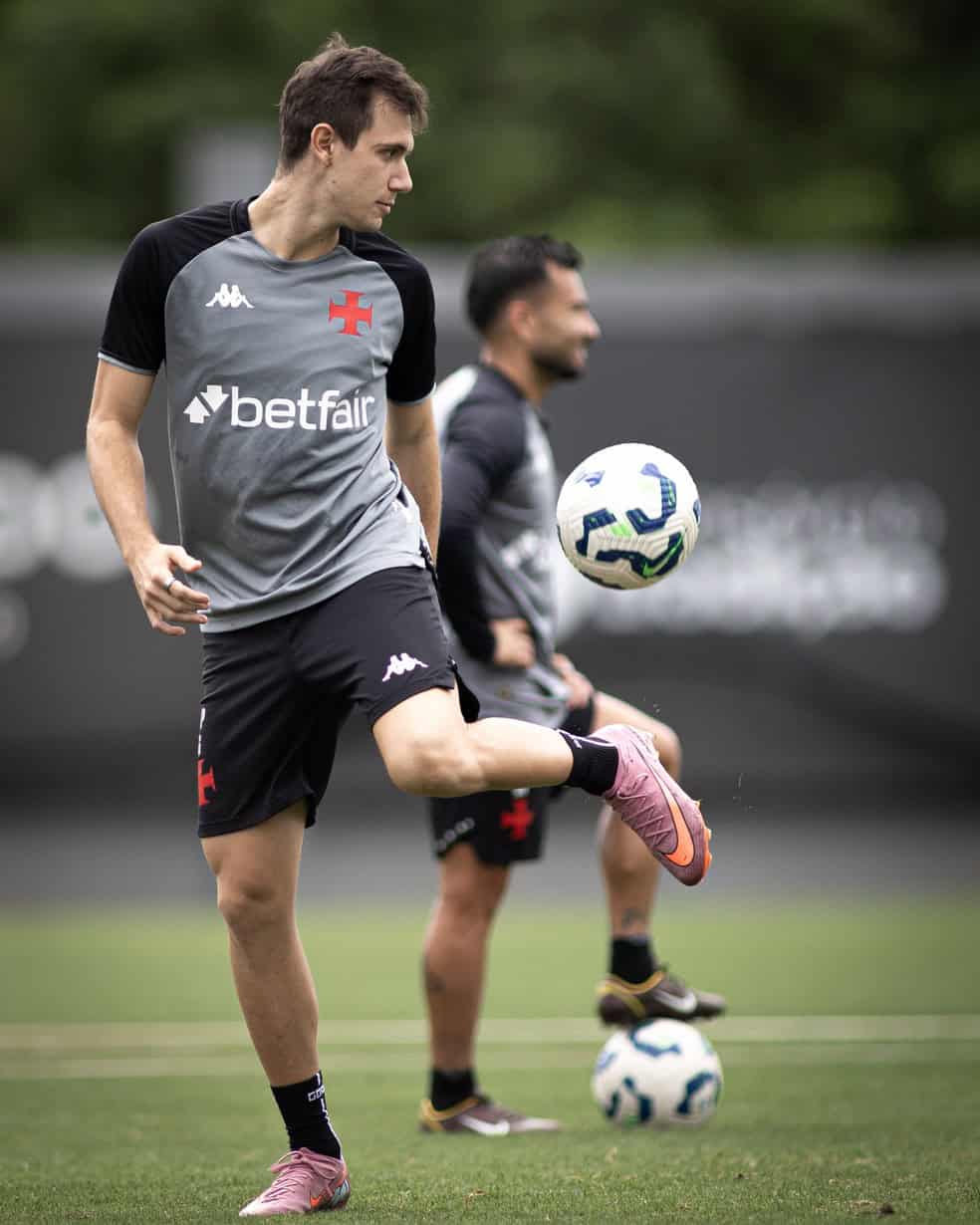 Jogador treinando com chuteira rosa, interceptando bola branca com detalhes azuis durante treino.