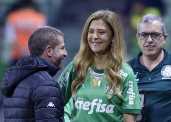 Árbitro e treinadores conversando no campo do estádio.