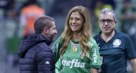 Árbitro e treinadores conversando no campo do estádio.