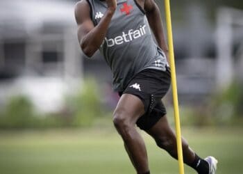 Atleta masculino treinando corrida com cones em campo ao ar livre.