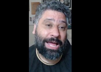 Homem com barba e cabelo cacheado sorrindo.