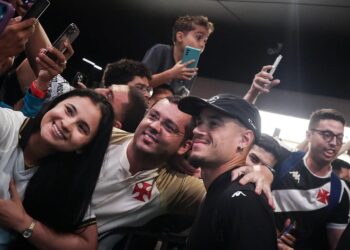 Fã sorridente com camisa do Vasco em evento com outros torcedores.