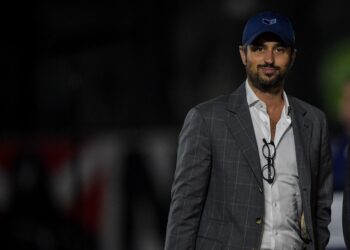 Vasco da Gama treinador em campo com traje formal e boné azul.