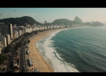 Vista aérea da orla de Copacabana, Rio de Janeiro, com o mar, praia e edifícios ao fundo.