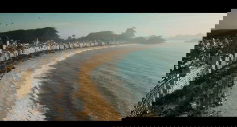 Vista aérea da orla de Copacabana, Rio de Janeiro, com o mar, praia e edifícios ao fundo.