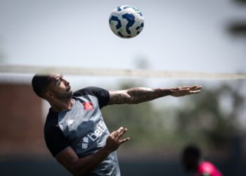 Bola de futebol no ar com jogador ao fundo.