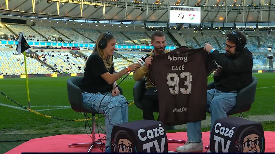 A imagem mostra três pessoas em uma entrevista no estádio do Vasco.