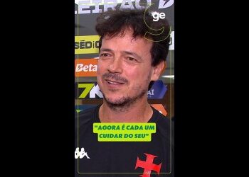 Homem com camiseta preta e fundo de banners esportivos.